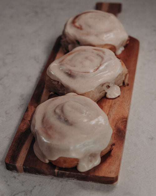 Three cinnamon rolls with icing on a wooden board on a light gray surface